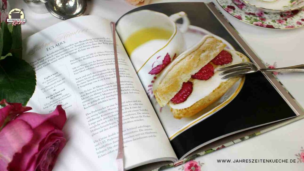 Das aufgeschlagene Buch A very british Teat Time zeigt das Rezept für Sahne-Himbeer-Eclairs. Darauf liegt eina silberne Kuchengabel.