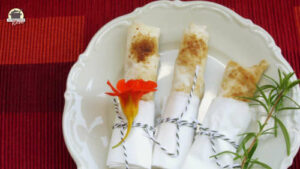 Auf einem Porzellanteller liegen drei süße Börek mit Aprikosen. Auf einem liegt eine Blüte der Kapuzinerkresse