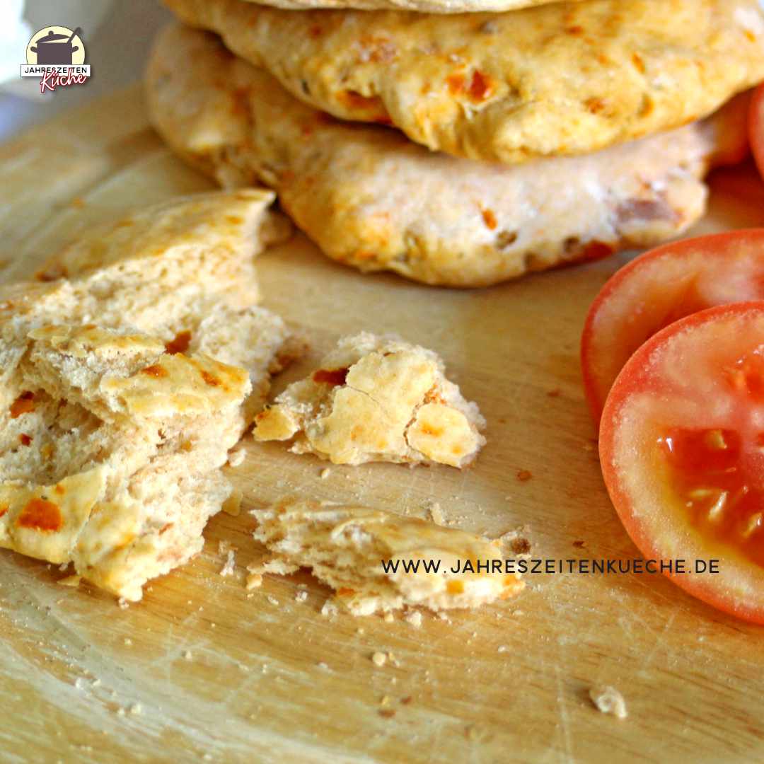 Auf einem Holzbrett liegen ein Stück Tomaten-Ciabatta und frische Tomaten.