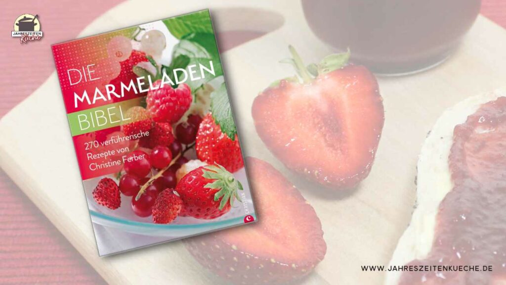 Aufgeschnitte Erdbeeren und ein Brötchen mit Marmelade liegen hinter dem Buch Die Marmeladen-Bibel von Christine Ferber