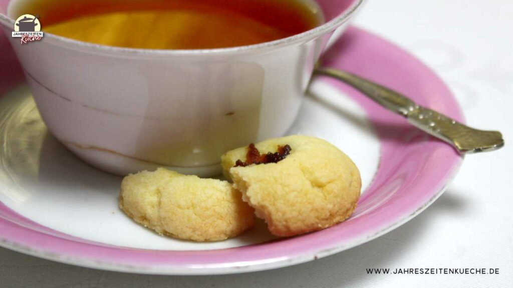 Neben einer Tasse Tee liegt ein Teelöffel und ein englischer Marmeladen-Keks