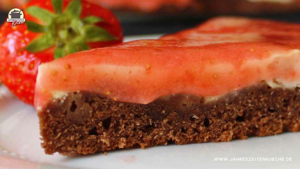 Ein Stück Marzipan-Käsekuchen mit Erdbeermark. Dahinter liegt eine Erdbeere