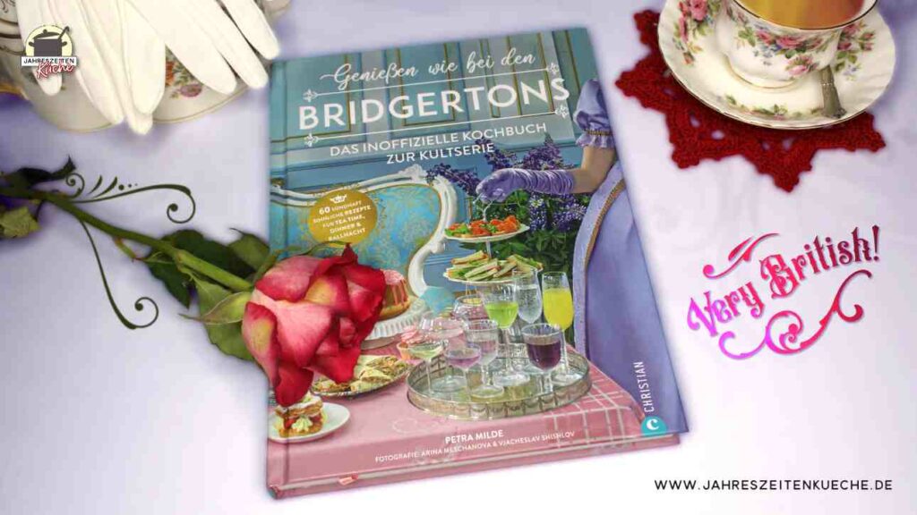 Auf dem Kochbuch Genießen wie bei den Bridgertons liegt eine Rose. Daneben steht eine Tasse Tee