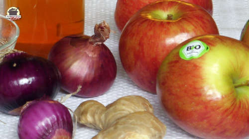 Auf einem weißen Tischtuch liegen die Zutaten für das Chutney Grundrezept: Essig, rote Zwiebeln, Äpfel und Ingwer
