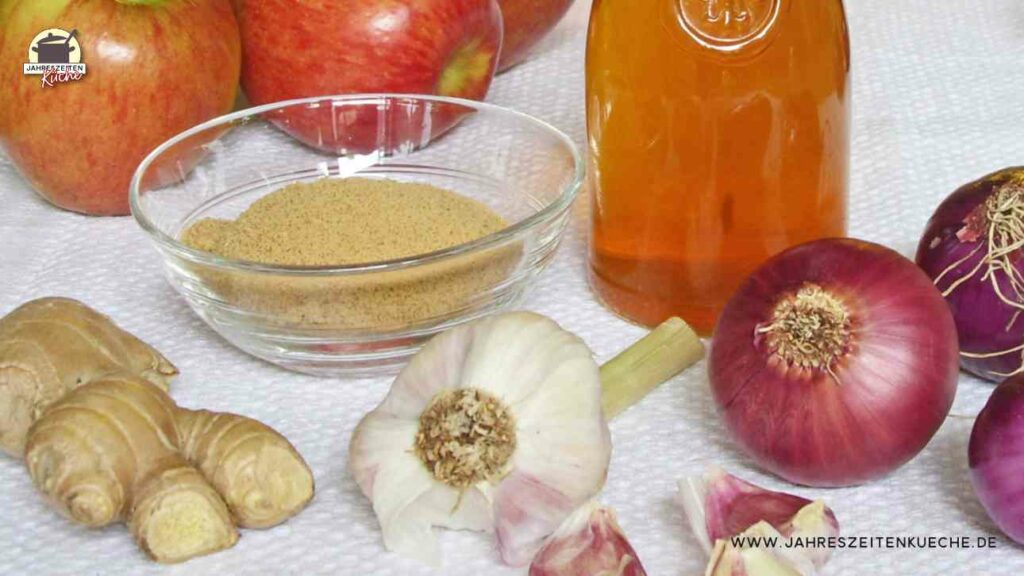 Bioäpfel, rote Zwiebeln, Ingwer eine Karaffe mit Essing stehen auf einem Tisch