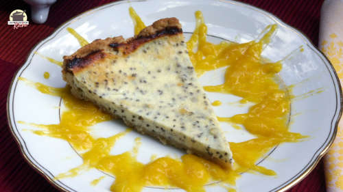 Auf einem weißen Teller liegt ein Stück Chia-Käsekuchen, um das strahlenförmig Mangomus verteilt ist