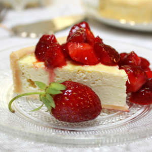 Ein Stück Käsekuchen mit versoffenen Erdbeeren liegt auf einem Glasteller.
