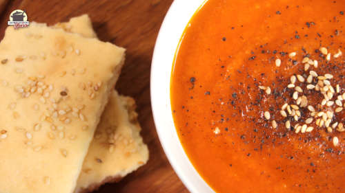 Neben einer weißen Suppenschale mit Karotten-Tomaten-Suppe liegt Lavashbrot.