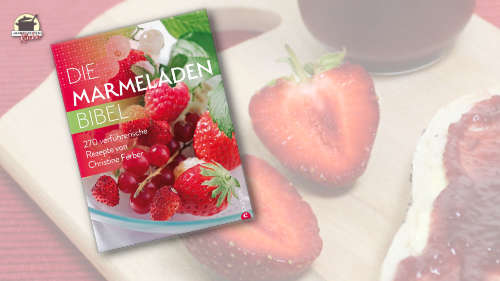Christine Ferbers Buch Die Marmeladen-Bibel ist im Vordergrund des Bildes. Im Hintergrund liegen Erdbeeren und ein halbes Brötchen mit Erdbeermarmelade