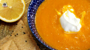 Auf einem Messingtablett stehen eine Zitrone, ein Stück Lavashbrot und eine Schale mit marokkanischer Karottensuppe.