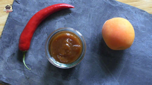 Auf einer Schieferplatte liegen eine rote Chilischote, eine Aprikose und ein kleines Glas Mirabellen-Aprikosen-Chutney
