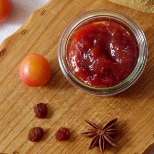 Neben einem Glas Wildpflaumen-Rosinen-Marmelade liegen eine Wildpflaumen, Rosinen und Sternanis