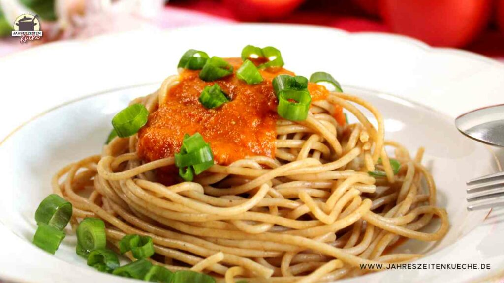 Spaghetti mit Paprika-Karotten-Soße. Darüber sind grüne Zwiebelringe gestreut.