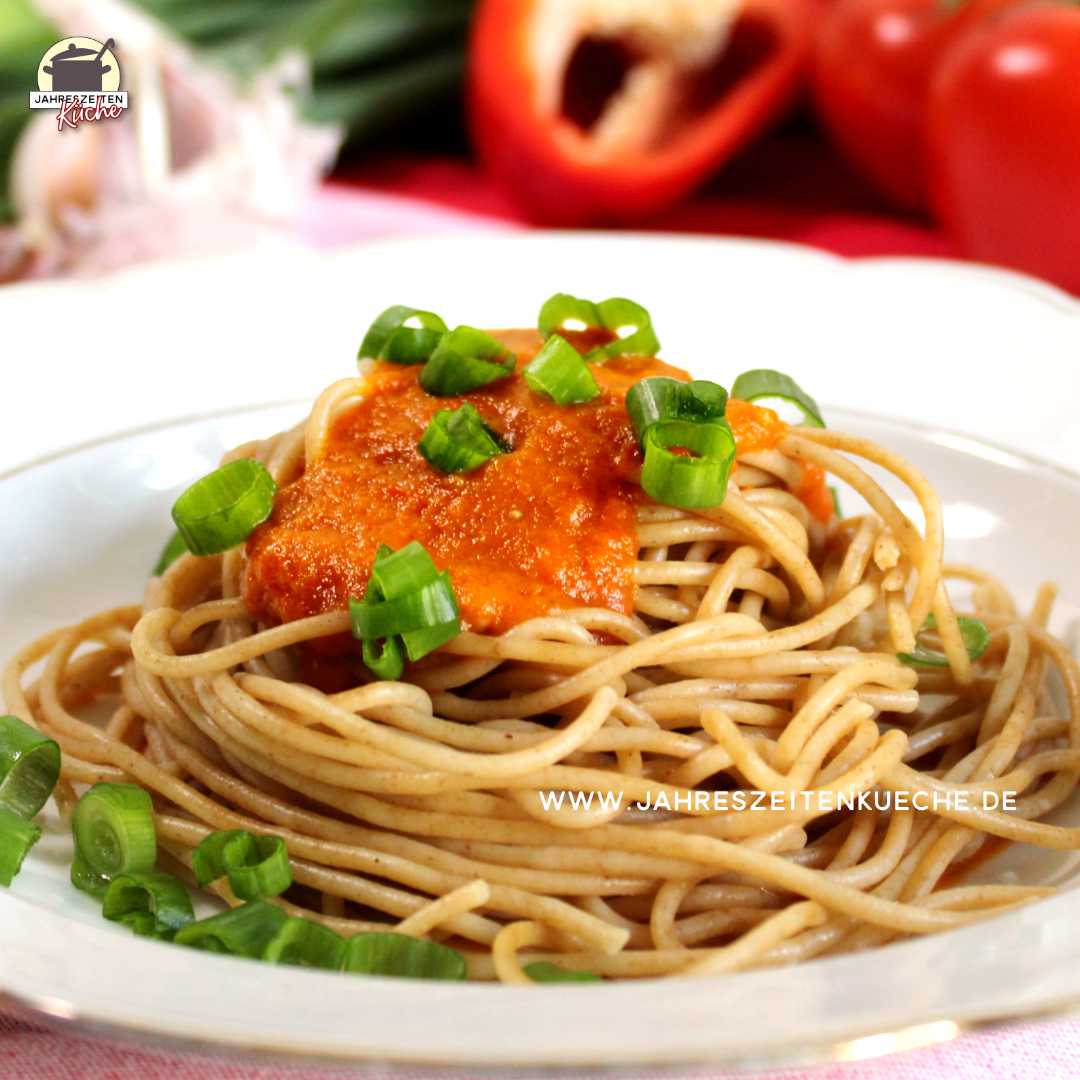 Spaghetti mit Paprika-Karotten-Soße. Darüber sind grüne Zwiebelringe gestreut.