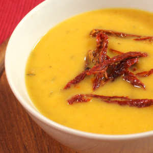 Streifen von getrockneten Tomaten garnieren eine sonnengelbe Pastinaken-Karotten-Suppe