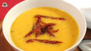 Orange-gelbe Pastinaken-Karotten-Suppe ist mit dunkelroten Tomatenstreifen dekoriert.