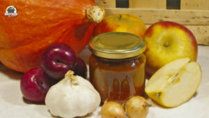 Kürbis, Pflaumen, Knoblauch, Zwiebeln, Apfel und ein Glas fertiges Chutney vor Kistenbrettern