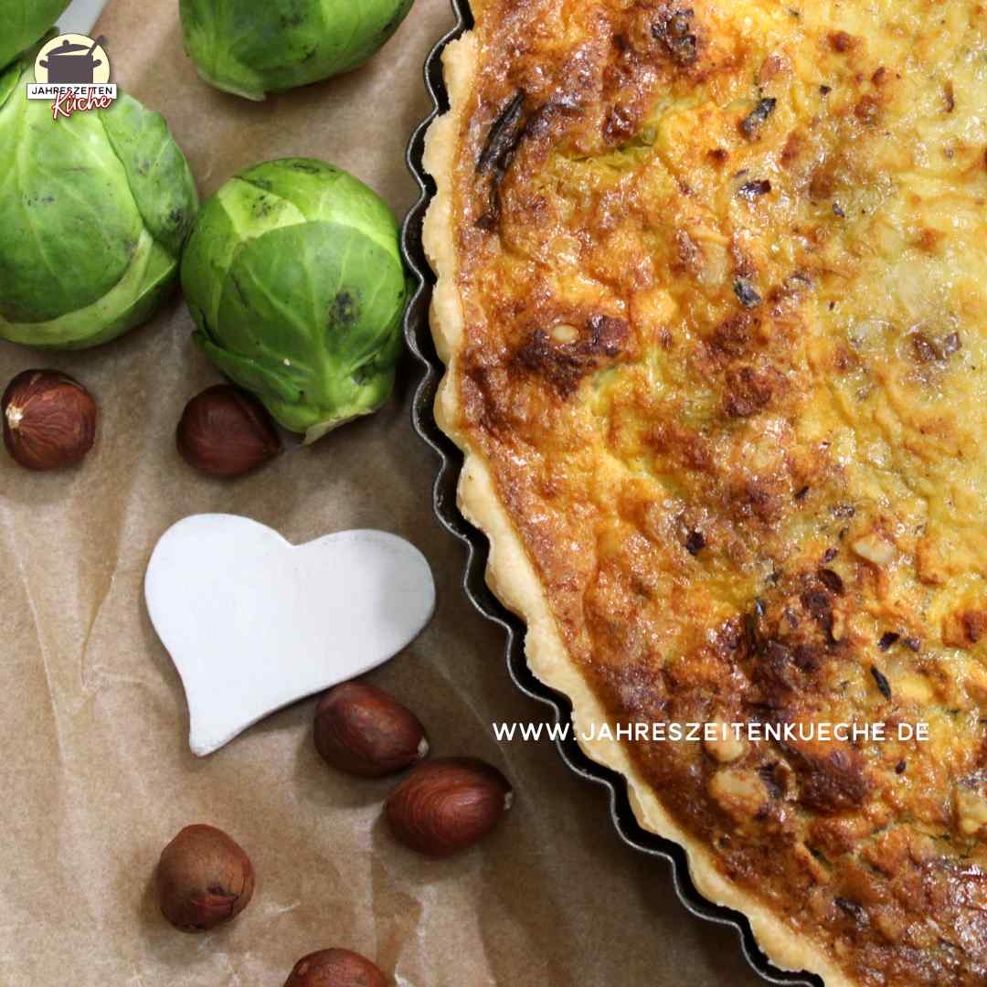 Neben einer Rosenkohl-Quiche liegen Haselnüsse, frischer Rosenkohl und ein kleines Herz.