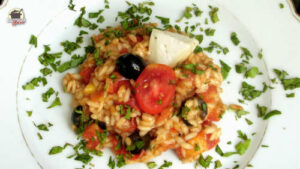 Auf einem weißen Teller ist eine Portion Risotto mit Tomaten und schwarzen Oliven angerichtet