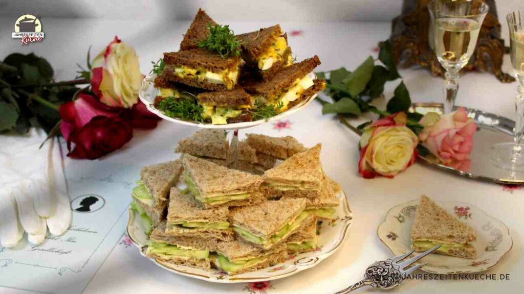 Auf einem weißen Tischtuch steht eine Etagere mit englischen sandwiches, ein Tabeltt mit Sherrygläser und frische Rosen