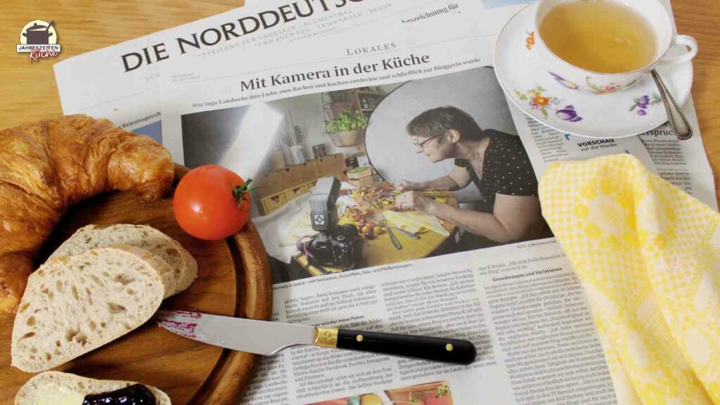 Zeitungsseite aus dem Weser Kurier vom 25.7.2022 mit einem BEricht über die Jahreszeitenküche. Darauf stehen eine Tasse mit tee und und ein Holzbrett mit Marmeladenbrot