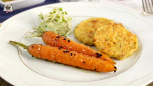 Auf einem weißen Teller liegen glasierte Karotten, Hüttenkäsepuffer und ein veganer Dip.