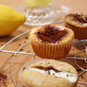 Auf einem Küchengitter stehen mehrere Zitronen-Muffins mit Stracciatella-Quark-Füllung