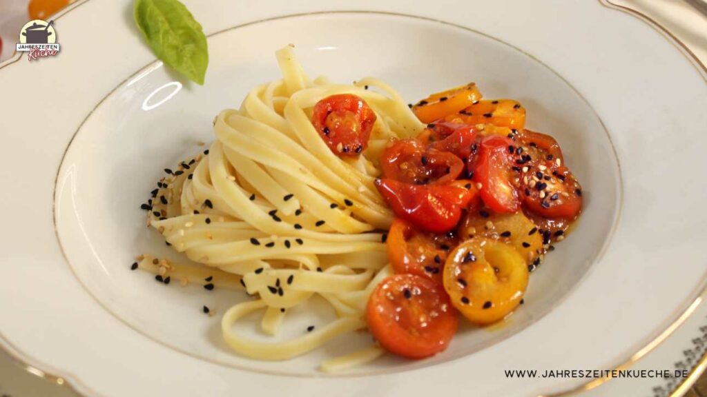 Auf einem weißen Teller sind Fettuccine mit glasierten Honig-Tomaten angerichtet.