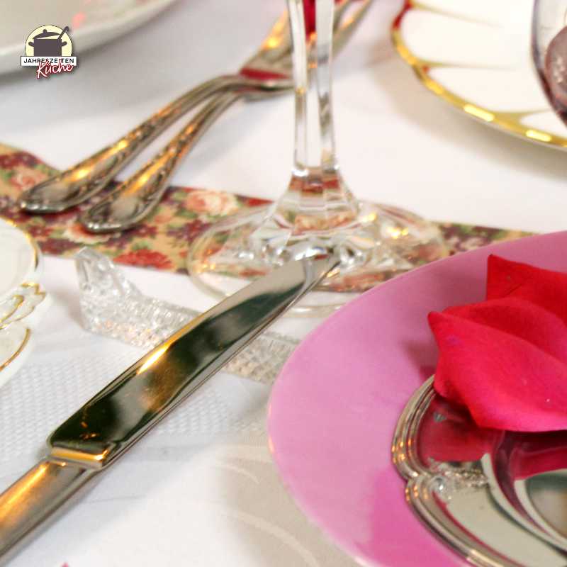 Glänzendes Besteck liegt neben einem Teller mit rosafarbenem Rand