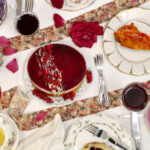 Ein reich gedeckter Tisch mit Gläsern, Tellern, Rotwein und Rosen