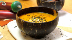 Eine schnelle Kürbissuppe in einer braunen Kokoschale ist mit Sesam und Schwarzkümmel bestreut