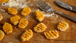 Mit der Gabel flach gedrückte Gnocchi liegen auf einer Holzplatte