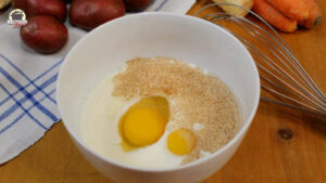 Eier und Milch in einer weißen Schüssel. Daneben liegt ein Schneebesen