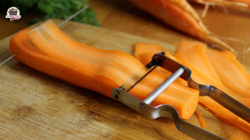 Karotte, von der mit einem Sparschäler dünne Scheiben abgeschnitten werden.