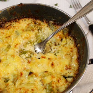 Überbackenes Käse-Lauch-Gratin in einer Pfanne. Darin steckt eine Gabel.