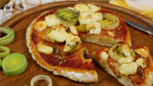 Eine Minipizza mit Lauch und Feta liegt auf einem runden Holzbrett