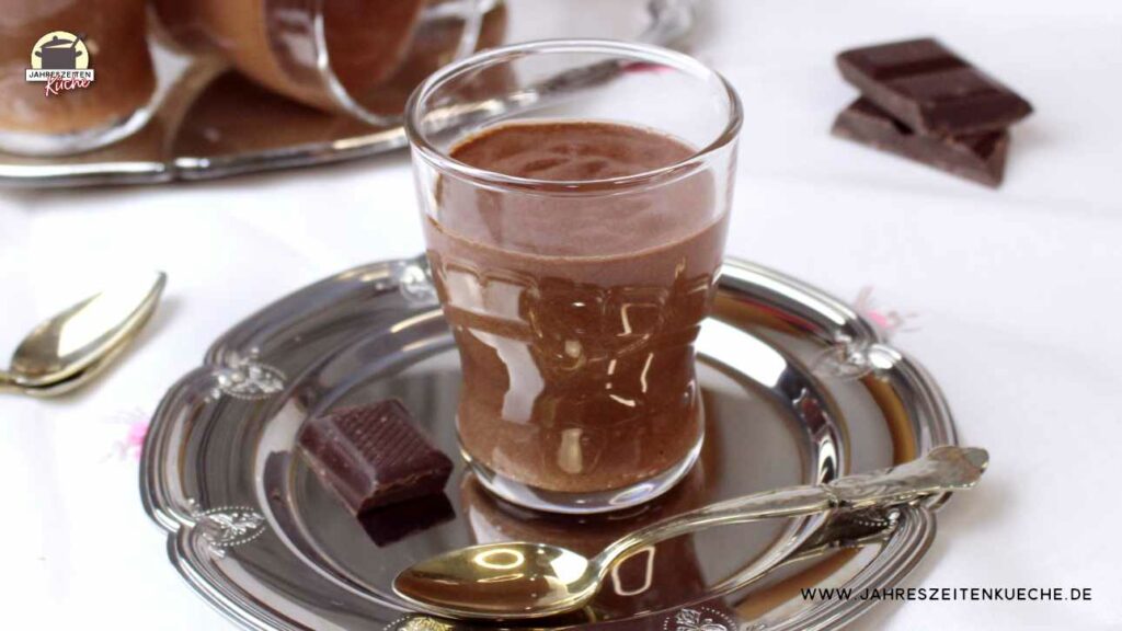 Auf einem silbernen Teller steht ein Glas mit Mousse au Chocolat. Daneben liegen ein kleiner Löffel und ein Stück Zartbitterschokolade