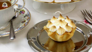 Auf einem silbernen Teller ist ein Lemon-Meringue-Pie. Links daneben steht eine Tasse Tee.
