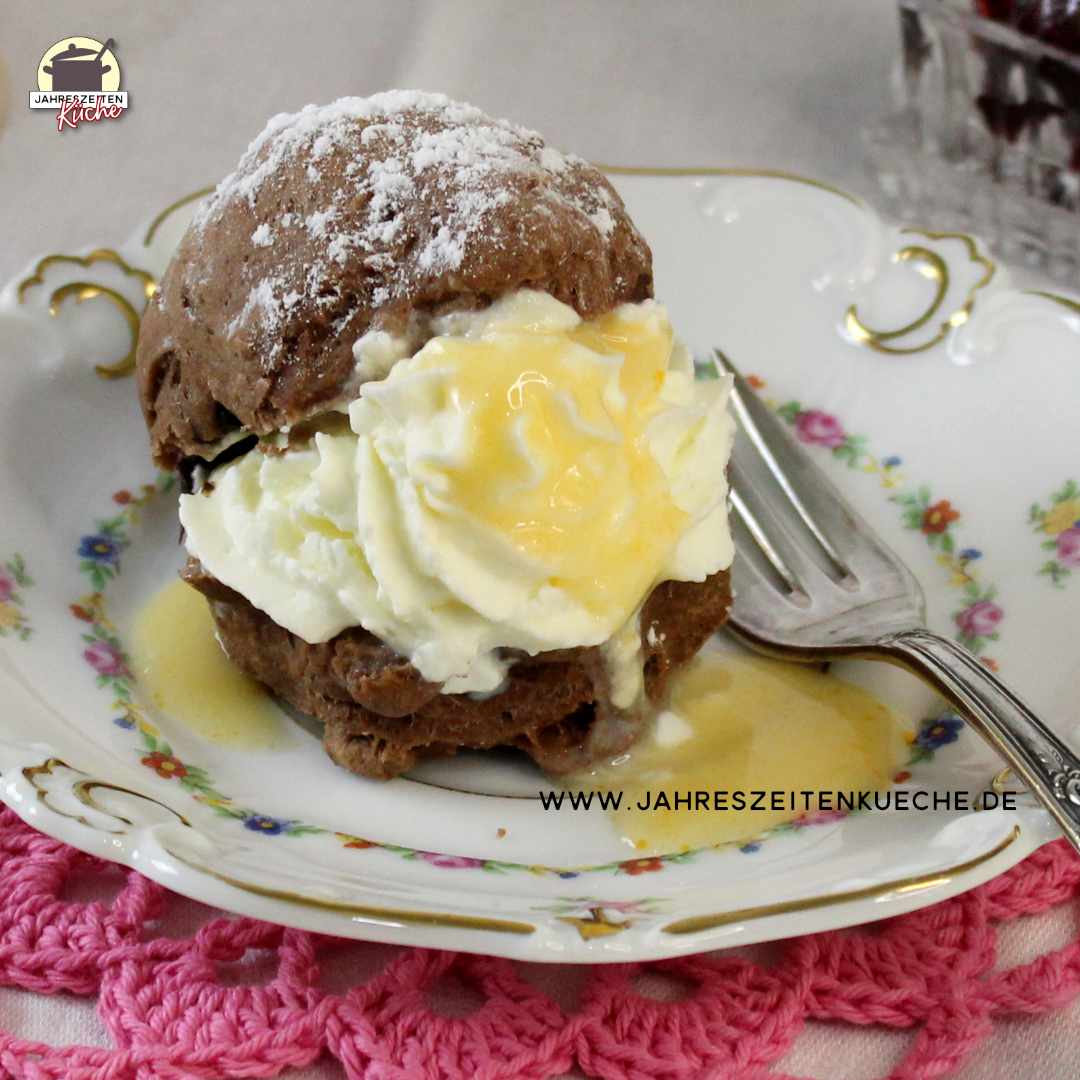 Auf einem geblümten Porzellan-Teller ist ein Schokoladen-Scone mit Schlagsahne und Eierlikör