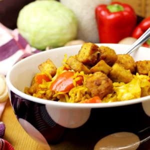 Reispfanne mit Weißkohl und Tempeh in einer Porzellanbowl, aus der eine Gabel steckt