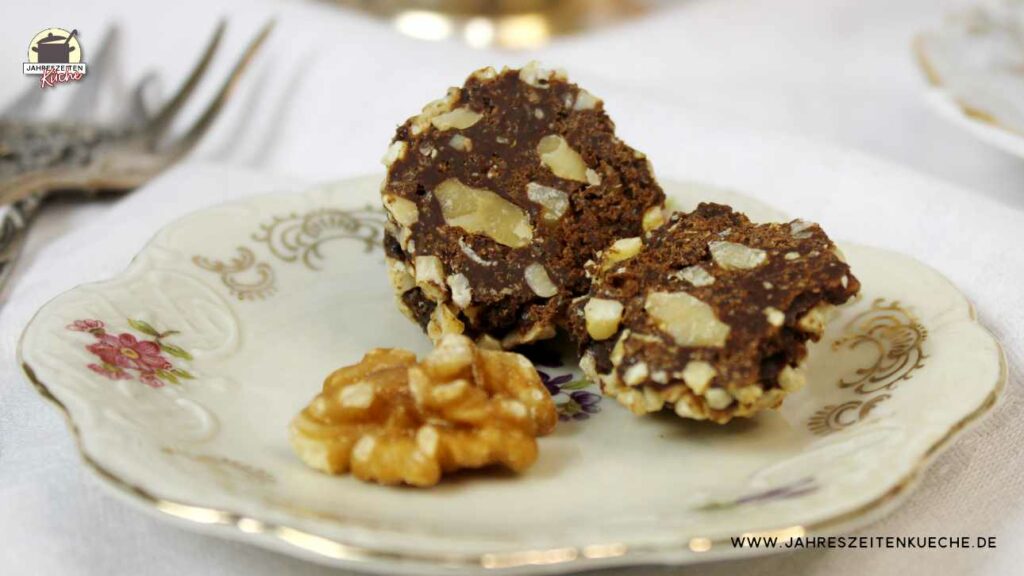 Eine Schokokugel ist in zwei Hälften geteilt und liegt zusammen mit einer Walnüsse auf einem kleinen Porzellanteller