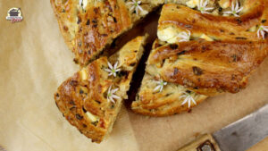 Gebackener Hefekranz mit Bärlauch und Feta bei dem ein Stück herausgeschoben wurde. bild in der Draufsicht.