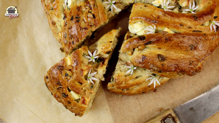 Gebackener Hefekranz mit Bärlauch und Feta bei dem ein Stück herausgeschoben wurde. bild in der Draufsicht.