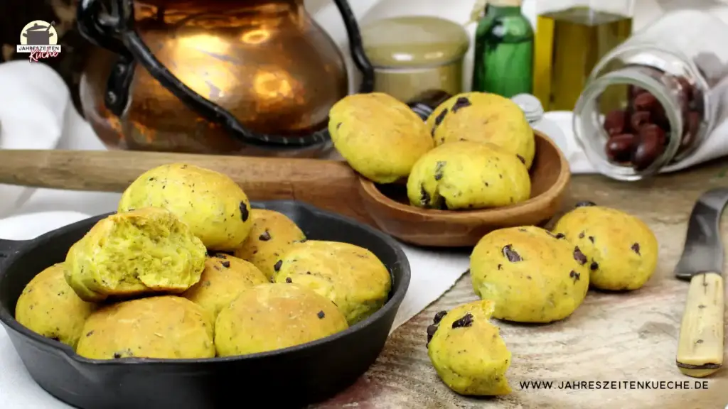 Im Vordergrund sind einige Partybrötchen mit schwarzen Oliven. Im Hintergrund steht ein alter Kupferkessel