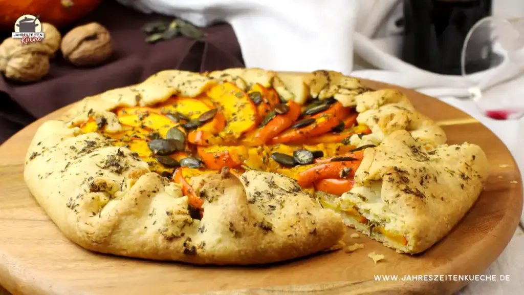 frisch gebackene Kürbis-Galette mit Kürbiskernen und Kräutern der Provence auf einem Holzteller