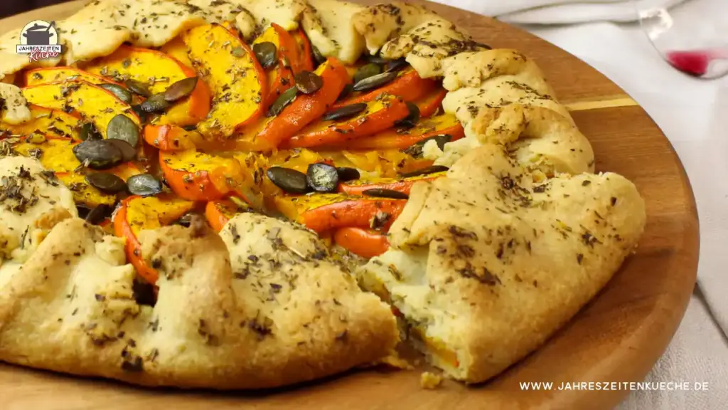frisch gebackene Kürbis-Galette mit Kürbiskernen und Kräutern der Provence auf einem Holzteller