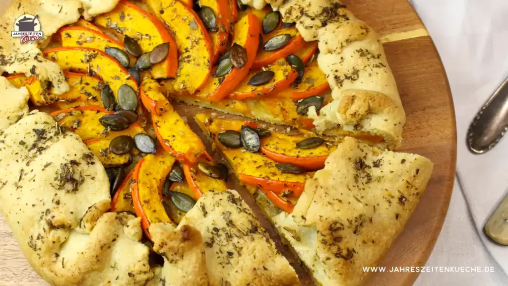 frisch gebackene Kürbis-Galette mit Kürbiskernen und Kräutern der Provence auf einem Holzteller