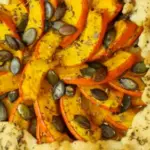 frisch gebackene Kürbis-Galette mit Kürbiskernen und Kräutern der Provence auf einem Holzteller