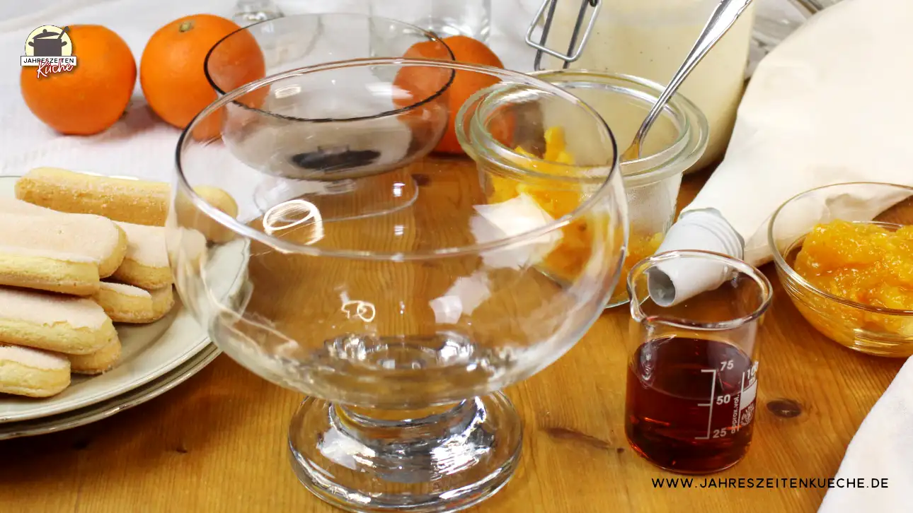 Auf einem Tisch stehen alle Zutaten für ein Orangen-Trifle: Löffelbisqits, Orangen, Amaretto, Sahne