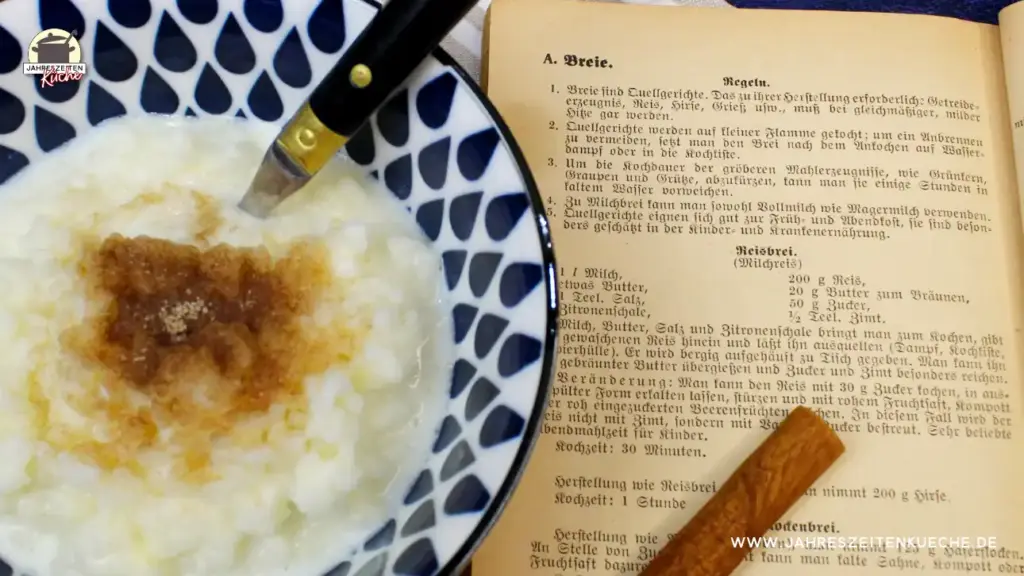 Eine blau-weiß gemusterte Schale in der Milchreis mit Zimt und Zucker ist. Daneben liegt ein altes Rezeptbuch